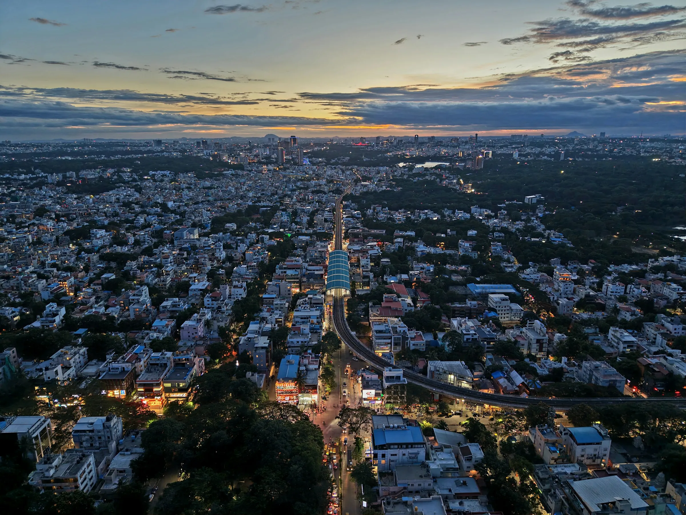 Aerial view of Bengaluru at dusk with the Metro line, residential neighbourhoods and city skyline