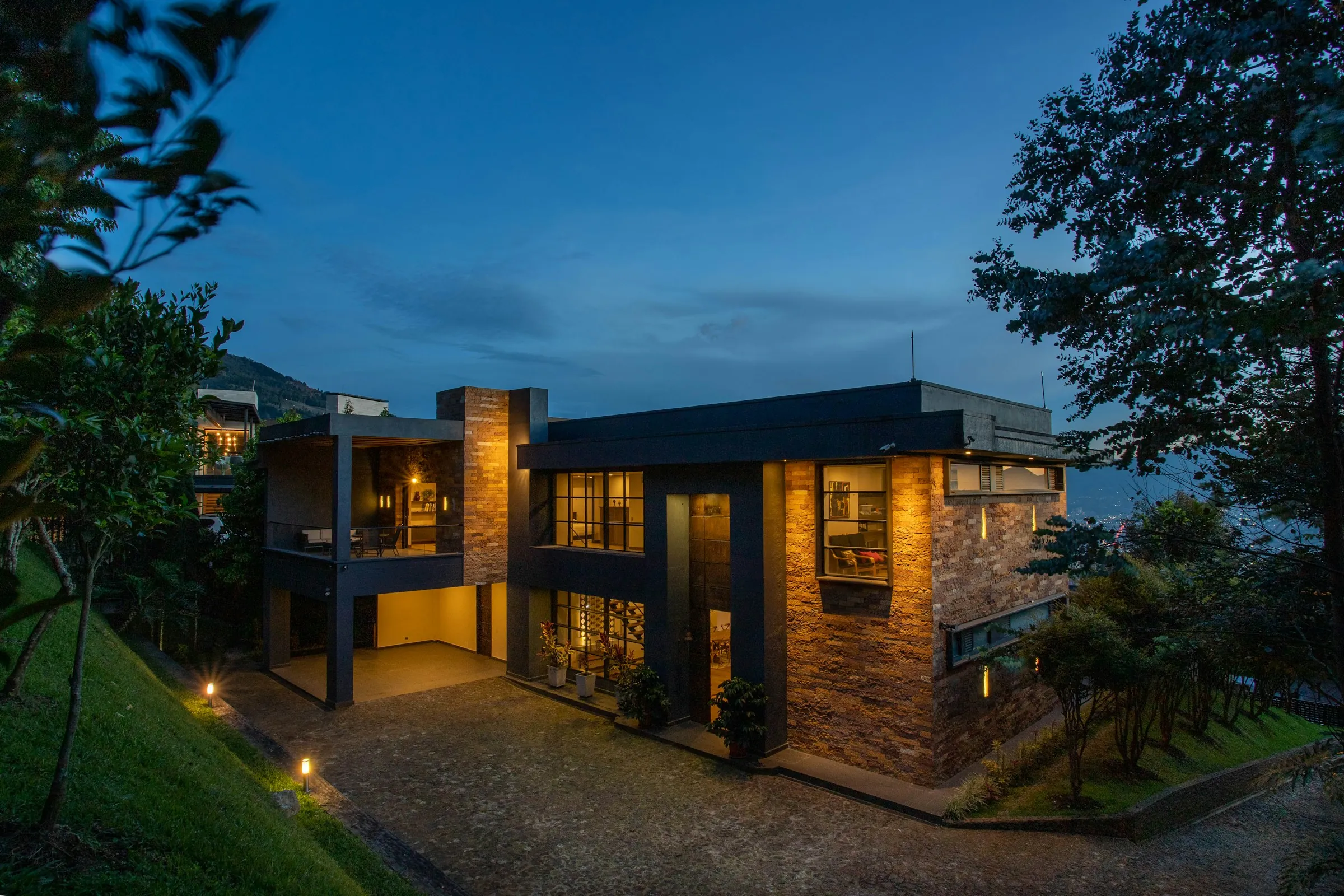 Contemporary stone-and-glass villa lit up at dusk with a landscaped garden
