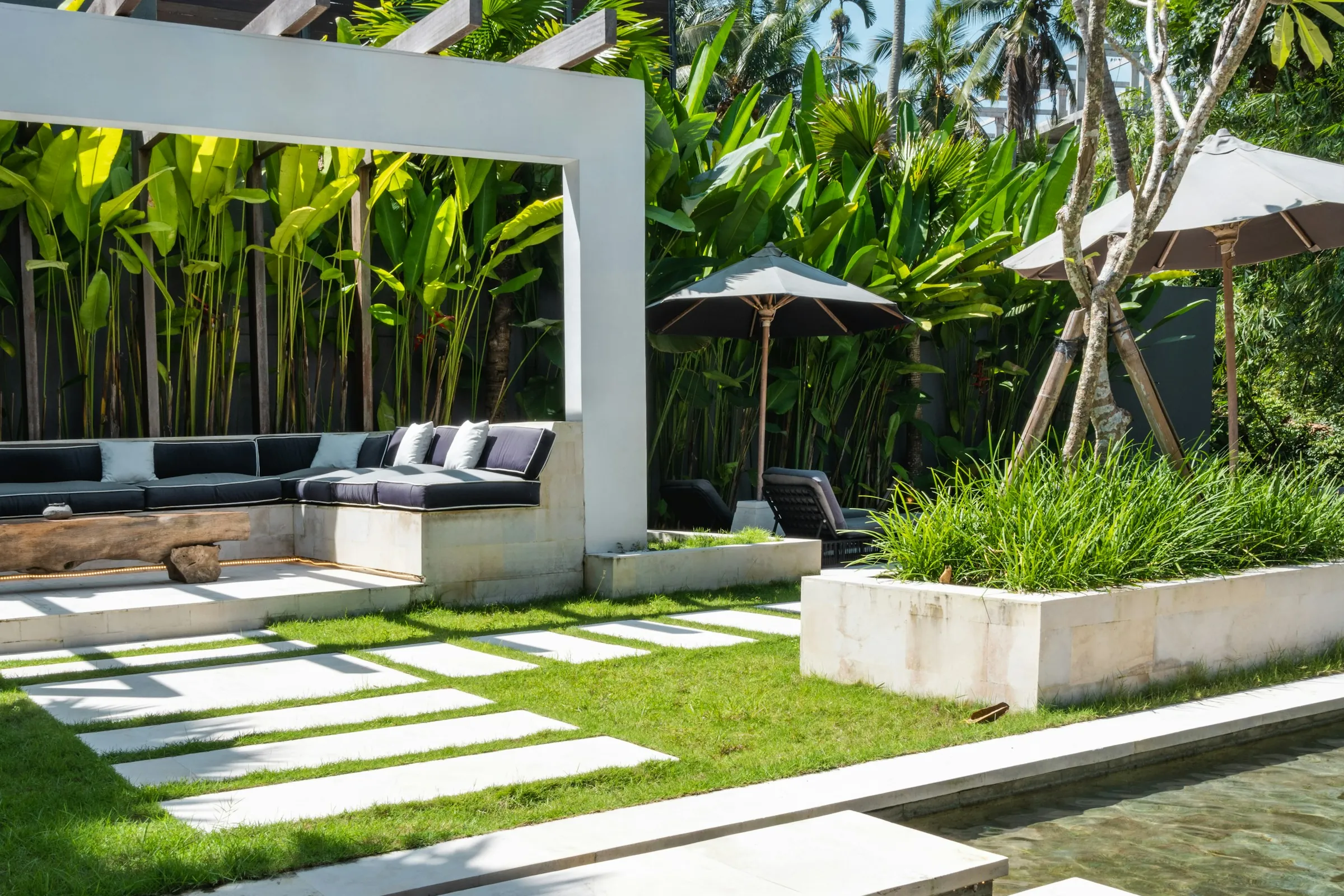 Tropical villa courtyard with pergola lounge, lawn and stepping stones over water